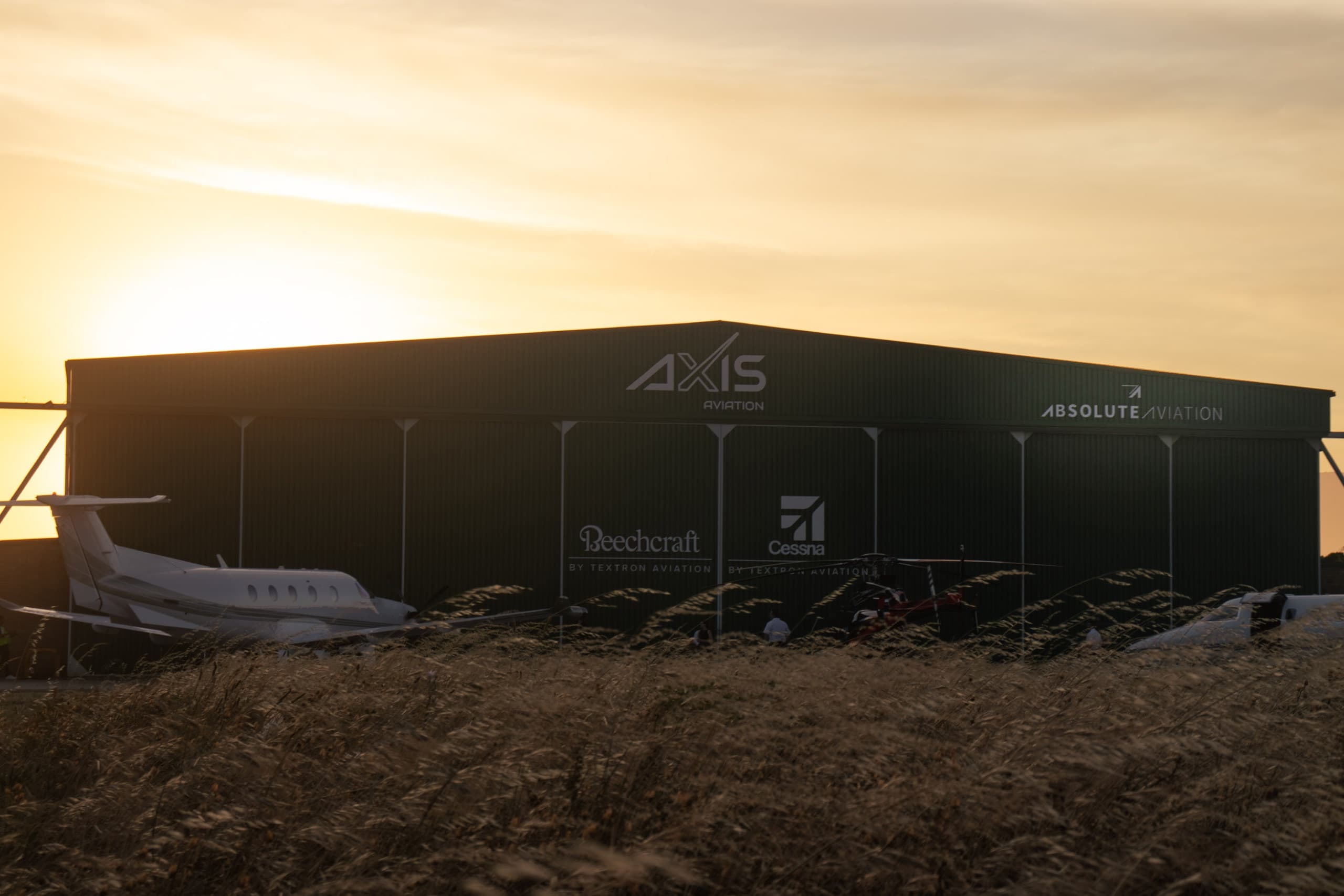 AXIS Aviation hangar silhouetted at golden hour with an aircraft nose in the foreground grass