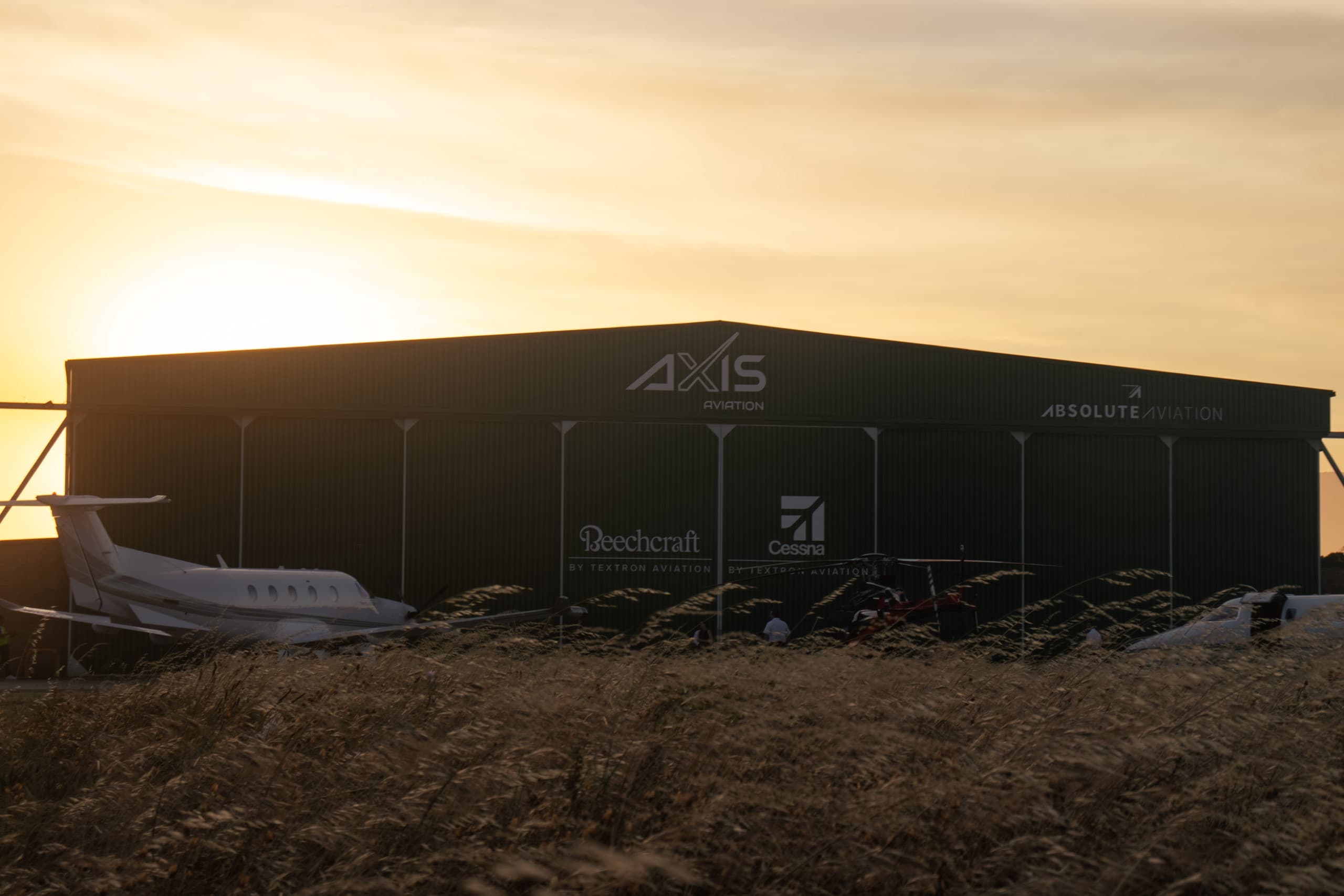 AXIS Aviation hangar silhouetted at golden hour with an aircraft nose in the foreground grass